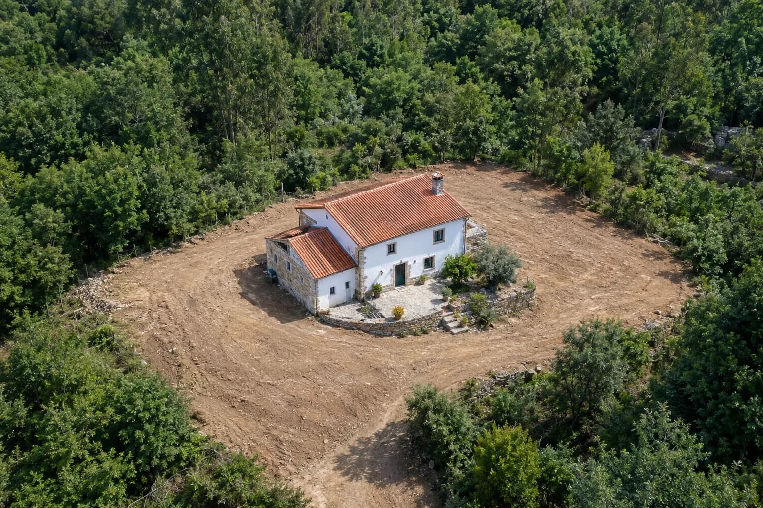 Vista aérea de uma moradia com faixa de terra limpa à volta, rodeada de mato