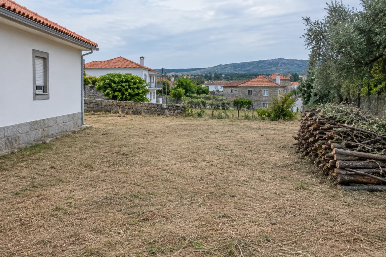 Terreno limpo e nivelado junto a uma casa, com mato cortado empilhado na berma